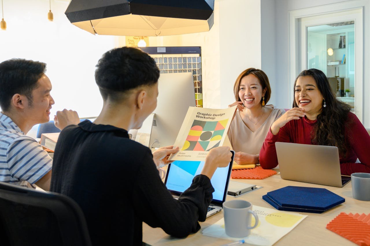 A diverse creative team in a lively meeting, discussing design ideas with laptops and a cheerful atmosphere.